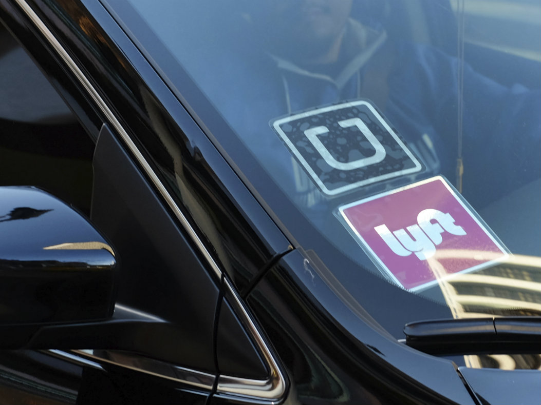In this Tuesday, Jan. 12, 2016, file photo, a driver displaying Lyft and Uber stickers on his front windshield drops off a customer in downtown Los Angeles.