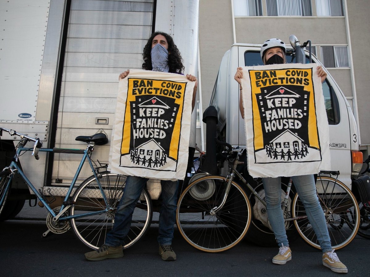 Galen Mancino, left, and Betsy Kinsey, hold up banners during a housing justice demonstration in the Adams Point neighborhood of Oakland on Dec. 5, 2020.