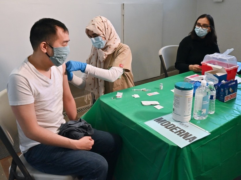 Justin Lau gets a bandage after his COVID-19 shot from UC Davis medical student Khadija Soufi as undergraduate Dana Hazem observes.