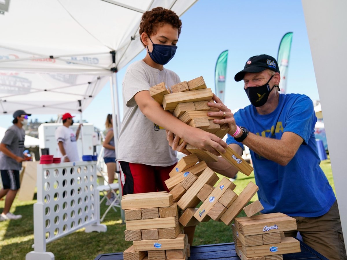 While wearing masks, David Bingener, 11, center, and Mark Bingener, right, play Jenga while tailgating before an NCAA college football game between the Hawaii Warriors and the UCLA Bruins, Saturday, Aug. 28, 2021, in Pasadena, Calif.