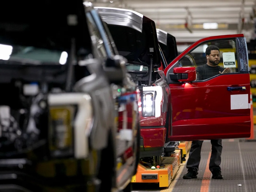 A worker adds a retail sticker to a newly assembled 2023 electric Ford F-150 Lightning on an assembly line at Ford's Rouge Electric Vehicle Center in Dearborn, Michigan.