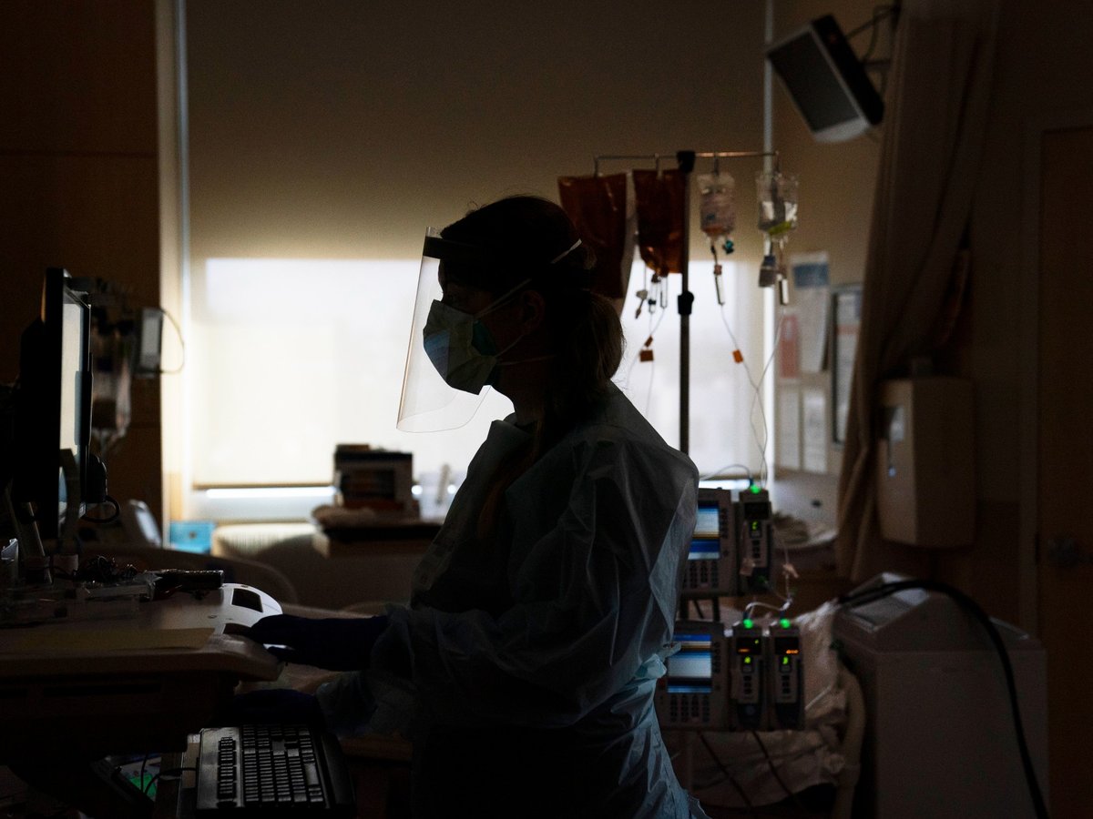 A registered nurse works on a computer while assisting a COVID-19 patient in Los Angeles.
