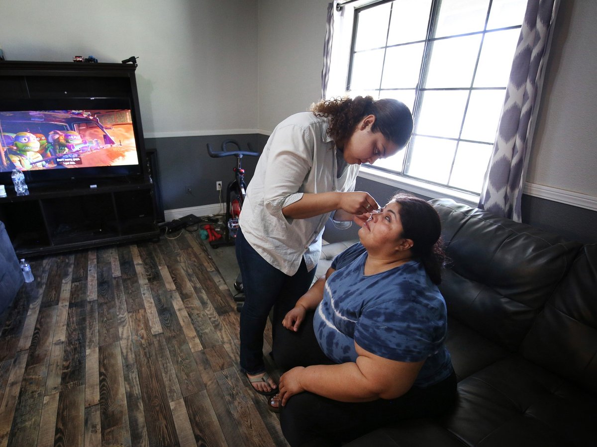 Marvin Estela Pineda, right, originally from El Salvador and blind from glaucoma, gets eye drops from her daughter Mayde at their home in Madera, Calif., Thursday, May 30, 2024.