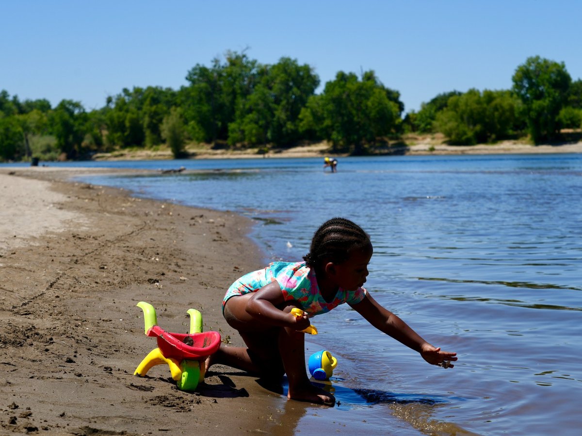 A young girl plays on the sand by the river in Sacramento, Calif., Tuesday, July 2, 2024.