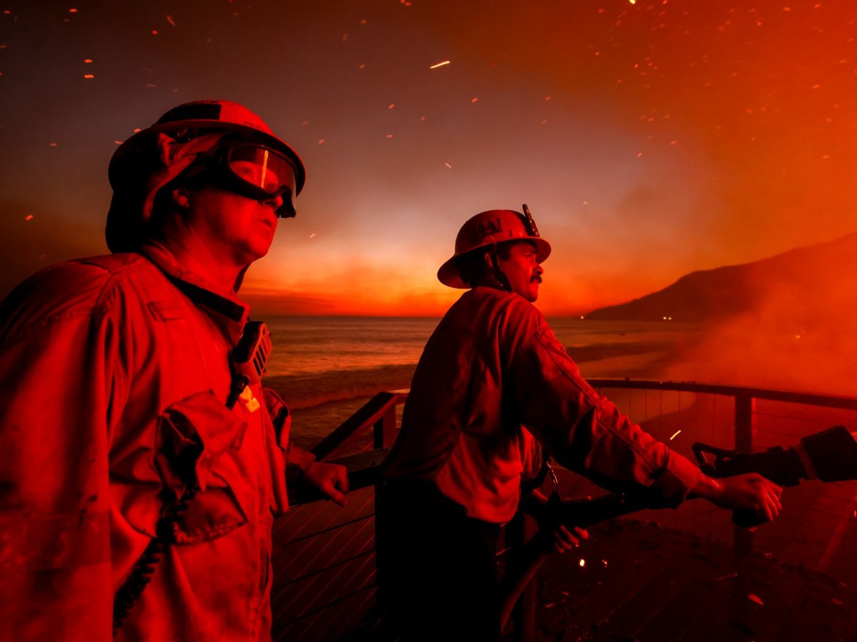 Firefighters work from a deck as the Palisades Fire burns a beachfront property Wednesday, Jan. 8, 2025 in Malibu, Calif.