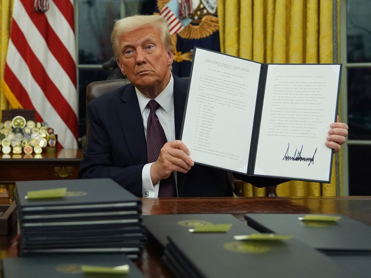 President Donald Trump holds up an executive order commuting sentences for people convicted of Jan. 6 offenses in the Oval Office of the White House, Monday, Jan. 20, 2025, in Washington.