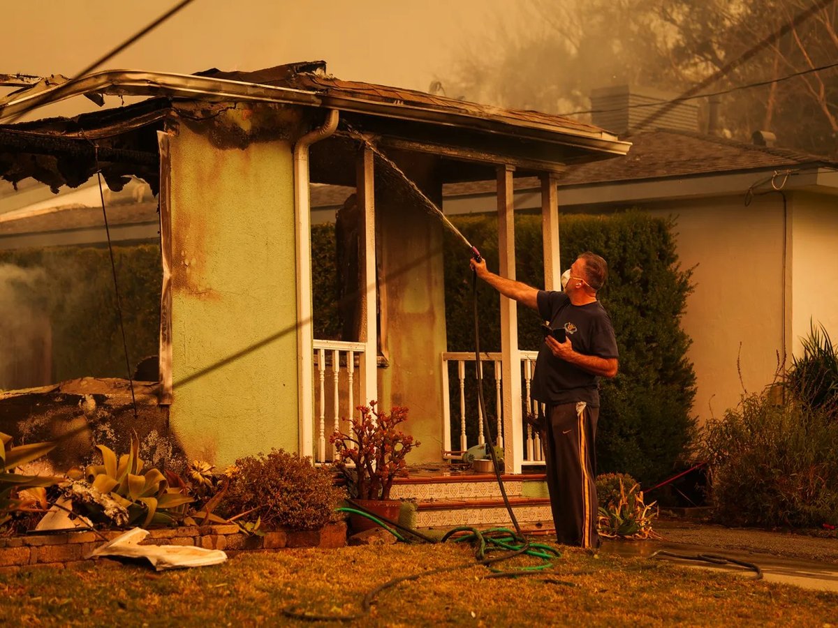 A person uses a hose to spray water on the flames of a house to prevent the Eaton Fire from spreading to other homes in Pasadena on Jan. 8, 2025. State Farm says losses from the fire have weakened its financial position.