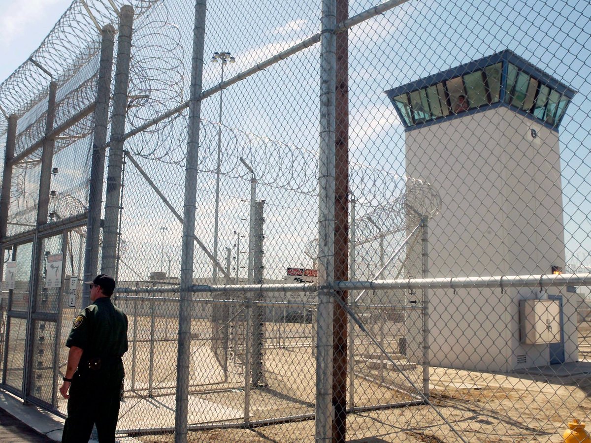 A correctional officer walks near a gate, which is one of two entrances into Kern Valley State Prison, June 14, 2005, in Delano, Calif.