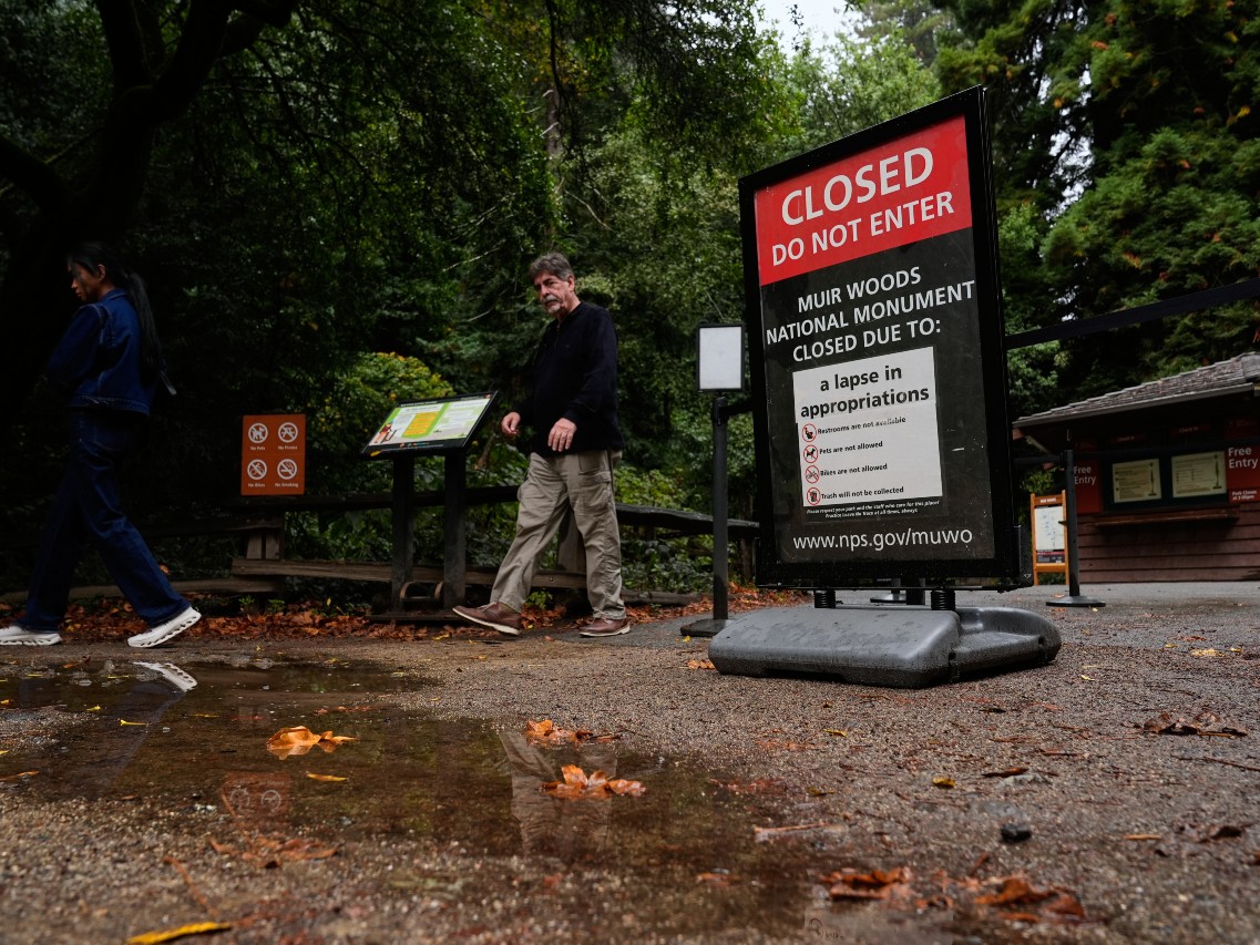 People walk past a sign notifying visitors that the Muir Woods National Monument is closed due to a government shutdown, Wednesday, Oct. 1, 2025, in Marin County, Calif.