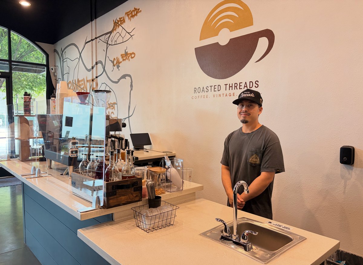 Angus West, owner of Roasted Threads, stands behind the counter at his coffee shop on April 22, 2026. West says even small cost increases can impact new businesses.