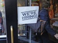 FILE - In this Wednesday, May 18, 2016, file photo, a woman passes a "We're Hiring!" sign while entering a clothing store.