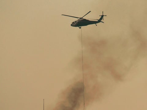 In this photo provided by the Santa Barbara County Fire Department, a helicopter makes a water drop near a house that was not on fire on a hill above Bella Vista Drive in Montecito, Calif.