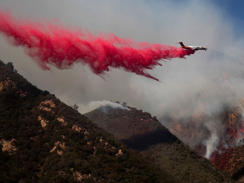 A plane drops fire retardant on a burning hillside Sunday, Nov. 11, 2018, in Malibu, Calif.