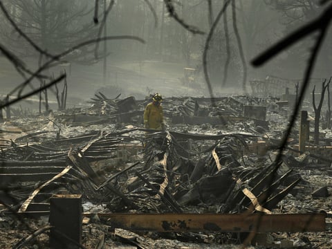 A firefighter searches a trailer park destroyed in the Camp Fire on Friday Paradise, Calif.