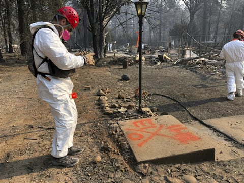 A volunteer member of an El Dorado County search and rescue team photographs the orange spray paint that marks the ruins of a home to show that no human remains were found at the location in Paradise, Calif., Sunday, Nov. 18, 2018.