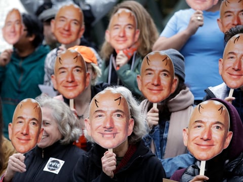 In this Oct. 31, 2018, file photo, demonstrators hold images of Amazon CEO Jeff Bezos near their faces during a Halloween-themed protest at Amazon headquarters over the company's facial recognition system, "Rekognition," in Seattle.