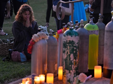 An attendee kneels in front of scuba tanks that were placed to represent each victim during a vigil Friday, Sept. 6, 2019, in Santa Barbara, Calif., for the people who died aboard the dive boat Conception.