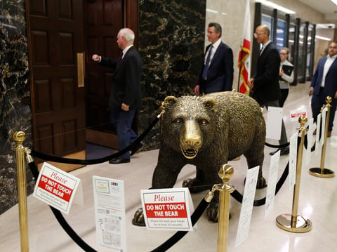 California Gov. Gavin Newsom, second from left, passes the sculpture of a bear outside his Capitol office, in Sacramento, Calif., Thursday, March 12, 2020.