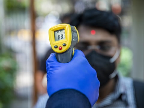 An office worker is screened with an infrared thermometer as he enters a building in New Delhi, India.