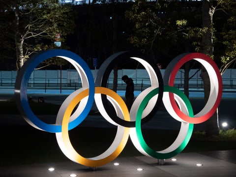 A man is seen through the Olympic rings in front of the New National Stadium in Tokyo, Tuesday, March 24, 2020.