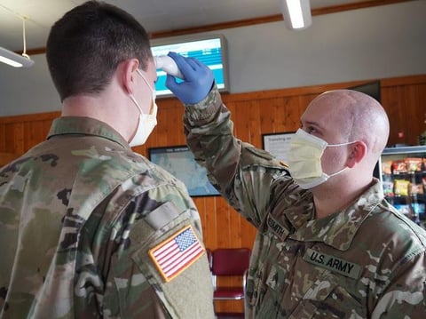 Army Sgt. Willy Nesmith from Cut Bank, Montana takes the temperature of Army Spc. Trevor Dodson as a part of daily personal wellness verification at the Amtrak Train Station in Shelby, Montana, April 3, 2020.