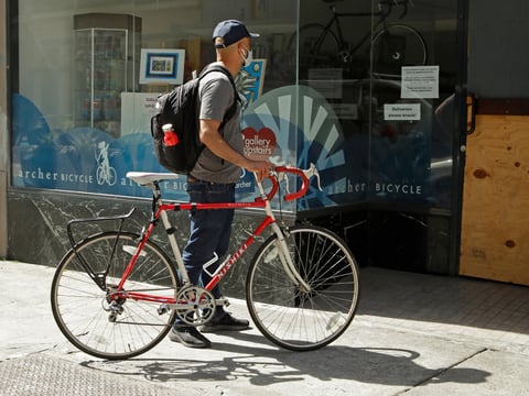 A man wearing a mask reads a notice on the window of Archer Bicycle shop on Thursday, May 7, 2020, in Oakland, Calif.