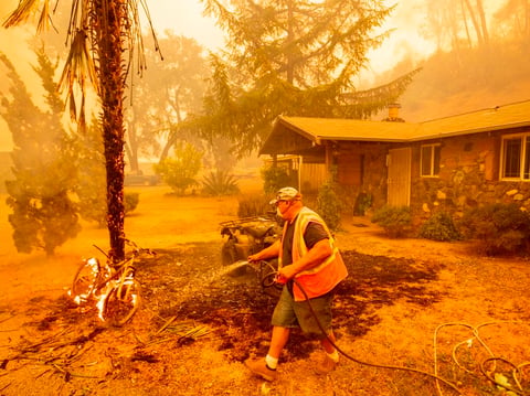 A Californian resident hoses down a burning bicycle and tree as flames from the Hennessey Fire approach a property in the Spanish Flat area of Napa, Calif., on Aug. 18.