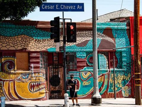 A man waits to cross the street in the largely Latino neighborhood of East Los Angeles on Aug. 7. California has implemented a new health equity metric to help address the outsize effect of coronavirus on the state's communities of color.