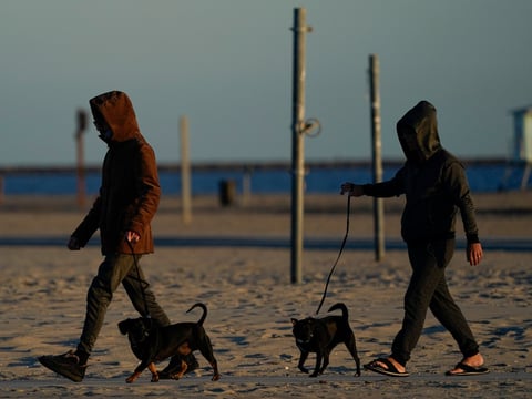 People wearing jackets walk their dogs on the beach Monday, Nov. 9, 2020, in Long Beach, Calif. Cooler temperatures moved through Southern California on Monday.