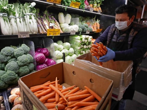 California grocery workers are pushing for stores to restore 'hero pay' as the pandemic drags on. In this file photo, a masked worker stocks produce at Gus's Community Market in San Francisco.