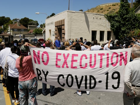 In this July 9, 2020, file photo, people hold up a banner while listening to a news conference outside San Quentin State Prison in San Quentin, Calif.