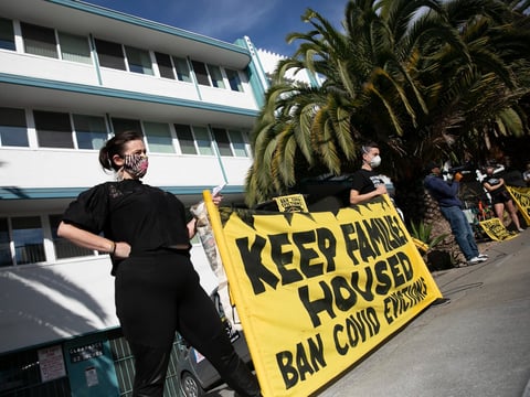Demonstrators hold up a banner in front of an apartment building in the Adams Point neighborhood of Oakland to protest rent payment and evictions during the coronavirus pandemic on Dec. 5, 2020.