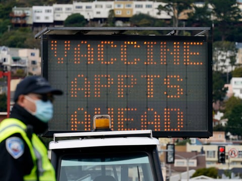 An officer stands in front of a sign advising of vaccine appointments at a drive-up vaccination center at City College of San Francisco during the coronavirus pandemic in San Francisco, Monday, Feb. 1, 2021.