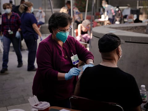 Registered nurse Julie Hurtado, left, administers the COVID-19 vaccine to a man in the courtyard of the Midnight Mission in Los Angeles, Wednesday, Feb. 3, 2021.