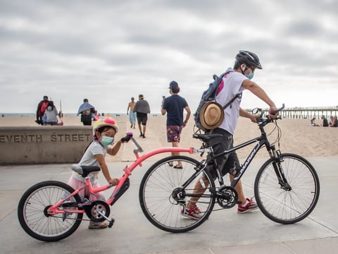 A girl and her father wear face masks while they push their bikes last summer in Hermosa Beach in the Los Angeles area.