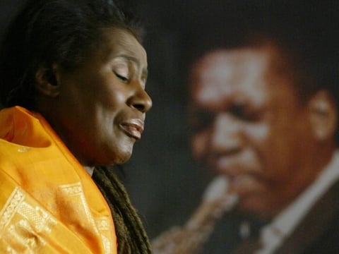 Alice Coltrane, widow of jazz great John Coltrane, playing the piano in her California home, in front of a portrait of her late husband.