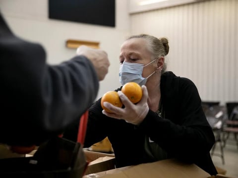 Food bank volunteer Betty Kimmel wears a protective mask as she hands out oranges to seniors in Martinez on March 19, 2020.