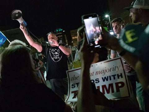 A man shouts into a bullhorn as Trump supporters gather in front of the Maricopa County Elections Department in Phoenix.