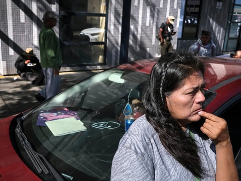 Angela Reyes Melo, 56, waits outside her car before driving to pick up supplies at a food bank on October 28, 2022, in San Diego. Reyes has been living with her son in a loaned car for the past four months.
