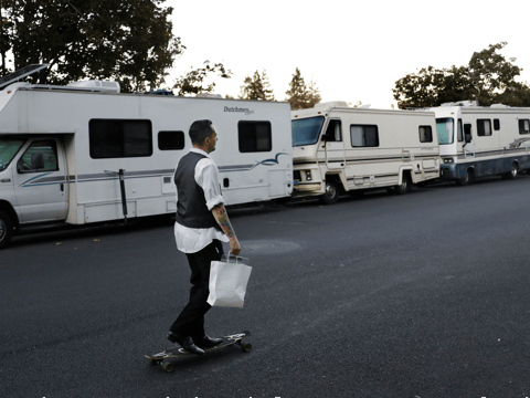 In this file photo taken Oct. 5, 2017, a man skates past a row of RVs where people live and sleep in the heart of silicon valley in Mountain View, Calif.