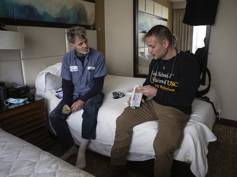 Patient Steven Dombrowski “Cowboy” speaking with Physician assistant Brett Feldman in his hotel room at the L.A. Grand Hotel on Feb. 13, 2023. The hotel was turned into an emergency shelter for unhoused people through Project Roomkey. Photo by Larry 