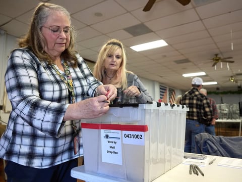 Poll workers Twyla Carpenter, left, and Regina Jasperse inspect the lock on a mail ballot drop box at a polling station at the American Legion in Shasta County on Nov. 7, 2023.