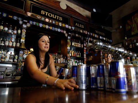 In this March 17, 2020, file photo bartender Courtney Schrag places beverage cans on the bar as she other employees prepare to close de Vere's Irish Pub in Sacramento, Calif.