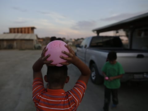 In this July 2, 2015 picture, Elias Trejo holds a water balloon over his head in front of his home in the community of Okieville, on the outskirts of Tulare, Calif.
