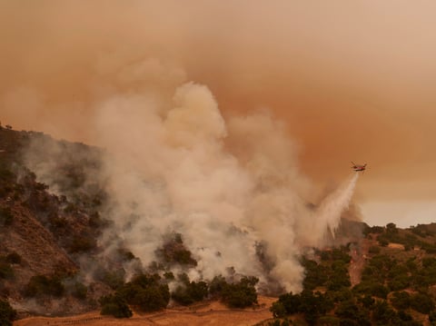 A water-dropping helicopter drops on flames from the advancing Lake Fire in Los Olivos, Calif., Saturday, July 6, 2024.