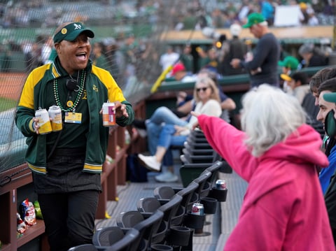 Derrick Smith, left, smiles as he delivers drinks for fans sitting in his section during a baseball game between the Colorado Rockies and the Oakland Athletics, Wednesday, May 22, 2024, in Oakland, Calif.