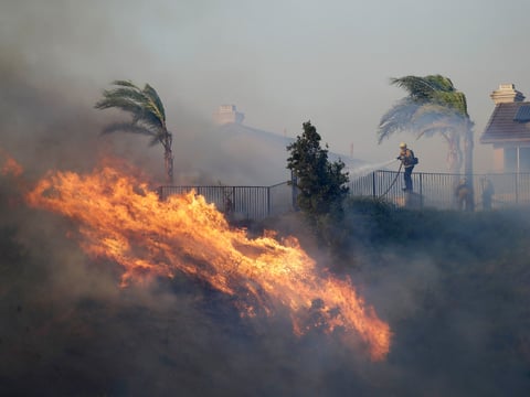 A firefighter sprays water in front of an advancing wildfire Friday, Oct. 11, 2019, in Porter Ranch, Calif.