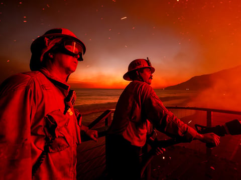 Firefighters work from a deck as the Palisades Fire burns a beachfront property Wednesday, Jan. 8, 2025 in Malibu, Calif.