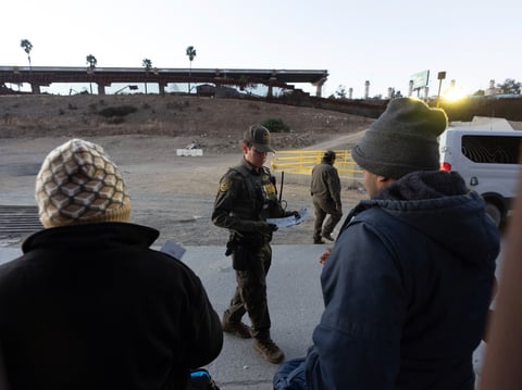 A Border Patrol agent hands out bag tags to a group of migrants waiting to apply for asylum between two border walls separating Mexico and the United States after crossing illegally, Tuesday, Jan. 21, 2025, in San Diego.