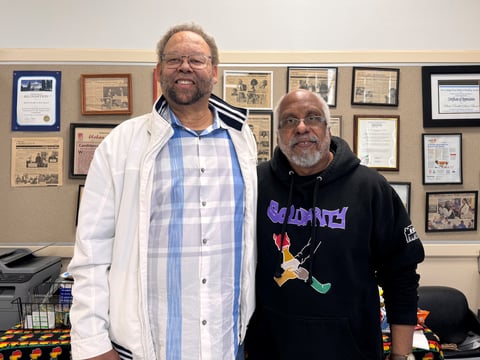 Darryl White and Carl Pinkston stand in front of news clippings about their work at the Black Parallel School Board headquarters in South Sacramento.